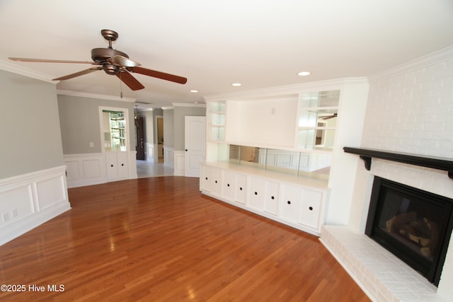 unfurnished living room with a decorative wall, a fireplace, wood finished floors, and crown molding