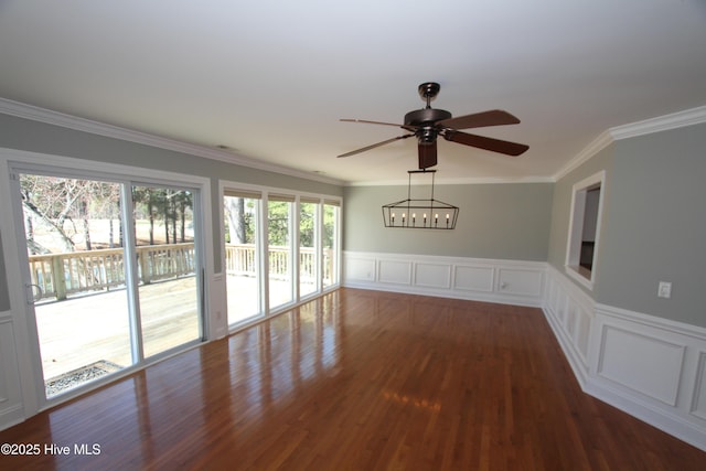 empty room featuring crown molding, a decorative wall, wainscoting, ceiling fan, and wood finished floors