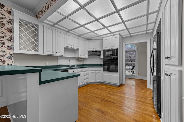 kitchen with black appliances, white cabinetry, and ventilation hood