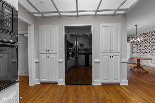 kitchen with black appliances, hanging light fixtures, wainscoting, and light wood-style flooring