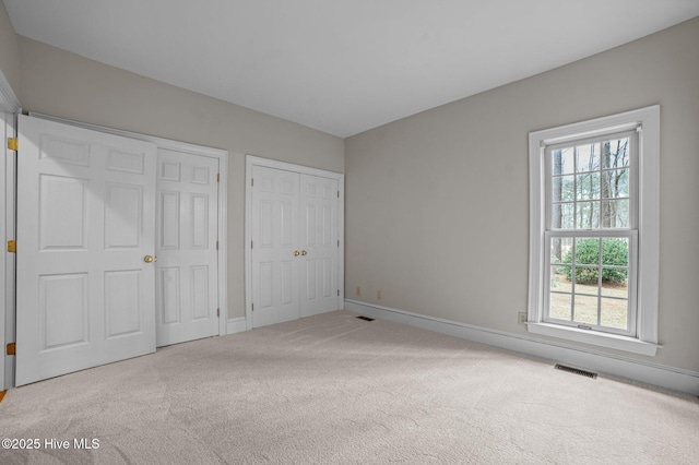 unfurnished bedroom with baseboards, carpet, visible vents, and multiple closets