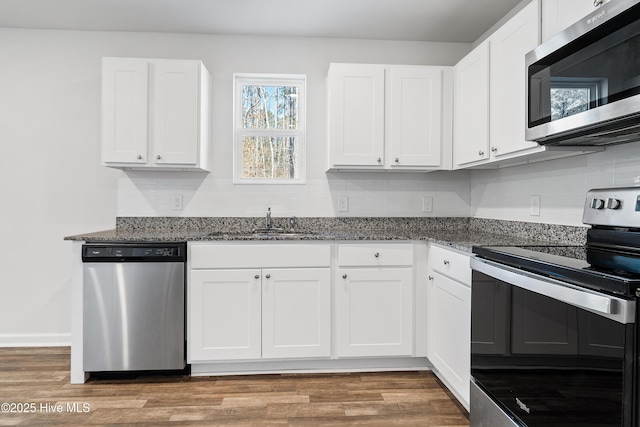 kitchen with stainless steel appliances, dark stone counters, white cabinetry, and a sink