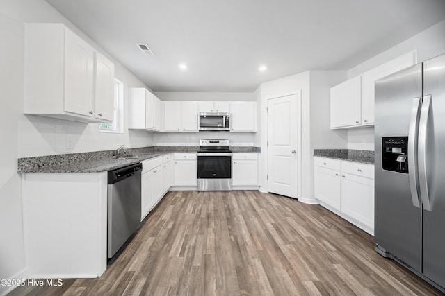 kitchen featuring visible vents, white cabinets, dark stone counters, stainless steel appliances, and a sink