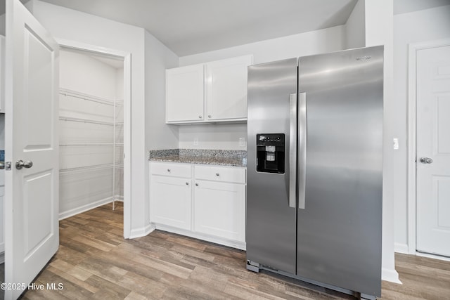 kitchen with dark stone countertops, light wood-type flooring, white cabinetry, and stainless steel fridge with ice dispenser