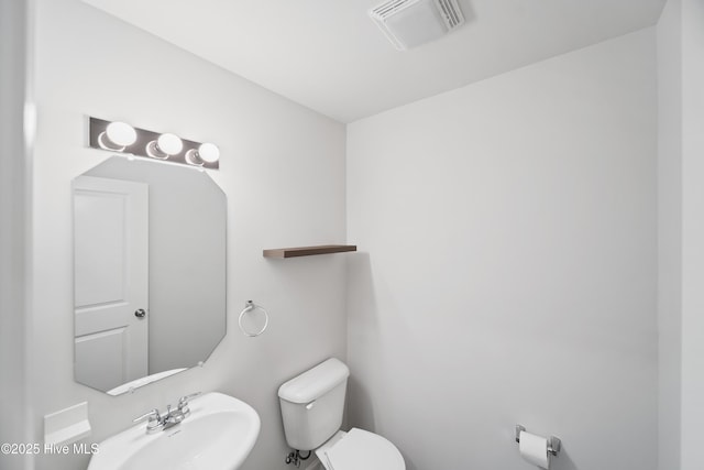 half bath featuring toilet, visible vents, and a sink