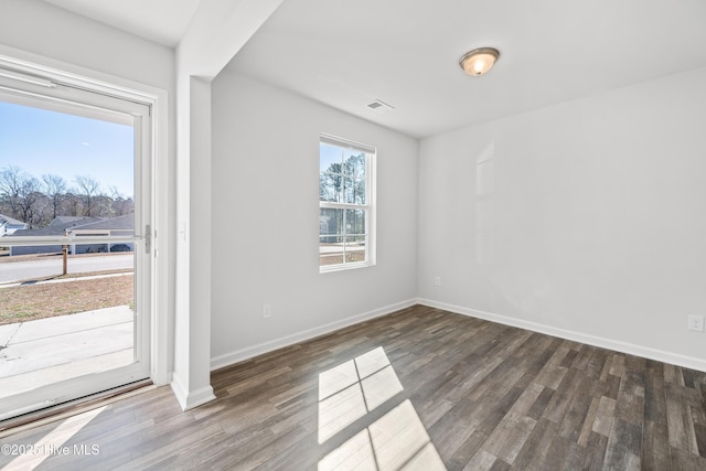 empty room featuring dark wood-style flooring, visible vents, and baseboards