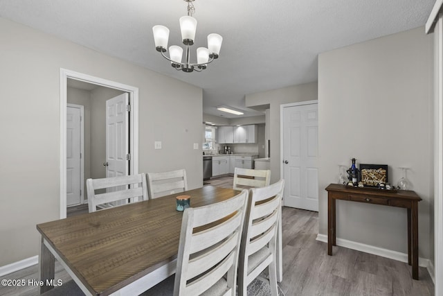 dining space featuring a notable chandelier, a textured ceiling, baseboards, and wood finished floors