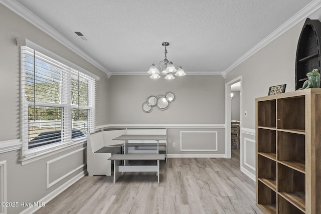 dining space with a chandelier, a textured ceiling, visible vents, light wood-style floors, and ornamental molding