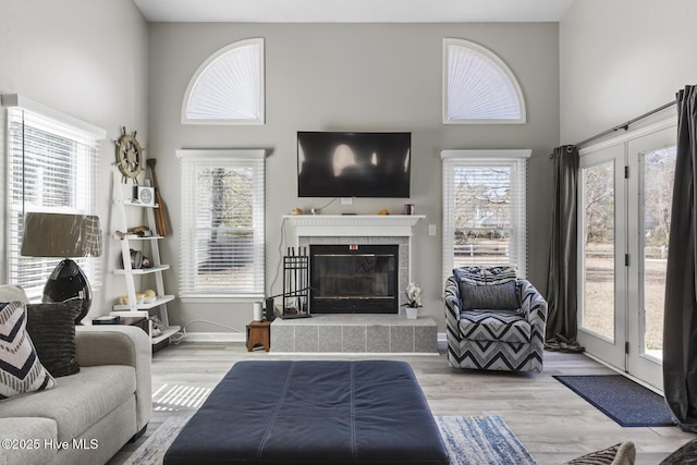 living room with a wealth of natural light, a high ceiling, a tiled fireplace, and light wood-style flooring