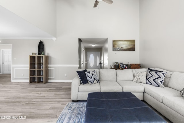 living room with a ceiling fan, a high ceiling, ornamental molding, and light wood finished floors