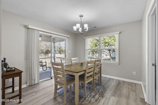 dining space featuring baseboards, a textured ceiling, light wood finished floors, and an inviting chandelier