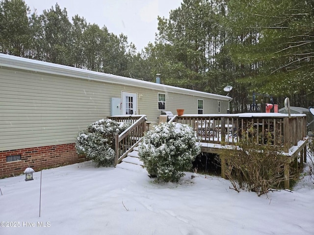 snow covered back of property with a deck and crawl space