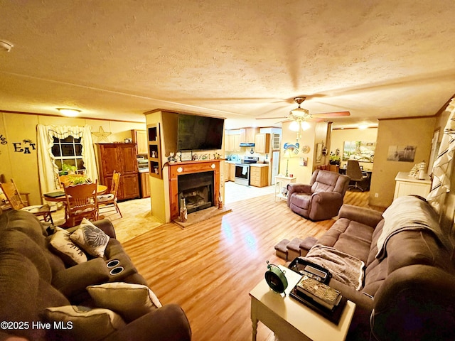 living area with a fireplace, ornamental molding, ceiling fan, a textured ceiling, and wood finished floors