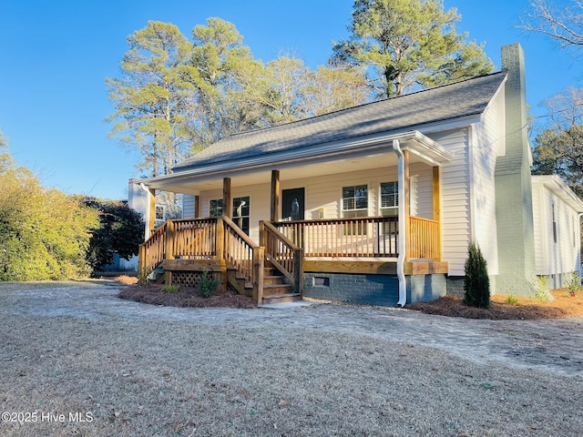 view of front of home with a porch, roof with shingles, and a chimney