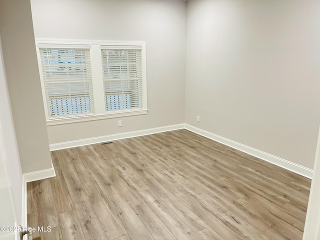 unfurnished room with light wood-type flooring, visible vents, and baseboards