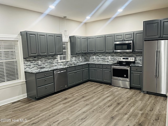 kitchen with appliances with stainless steel finishes, backsplash, gray cabinets, light stone countertops, and pendant lighting