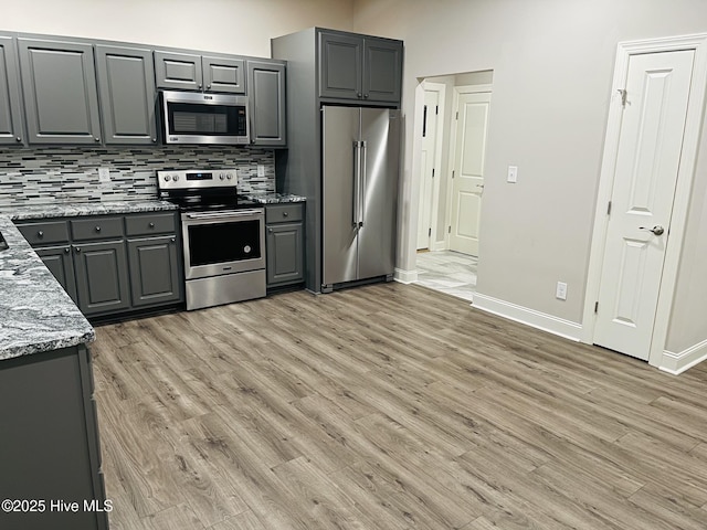 kitchen featuring light stone counters, light wood-style flooring, appliances with stainless steel finishes, gray cabinets, and decorative backsplash