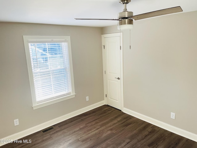 empty room featuring dark wood-style flooring, visible vents, and baseboards