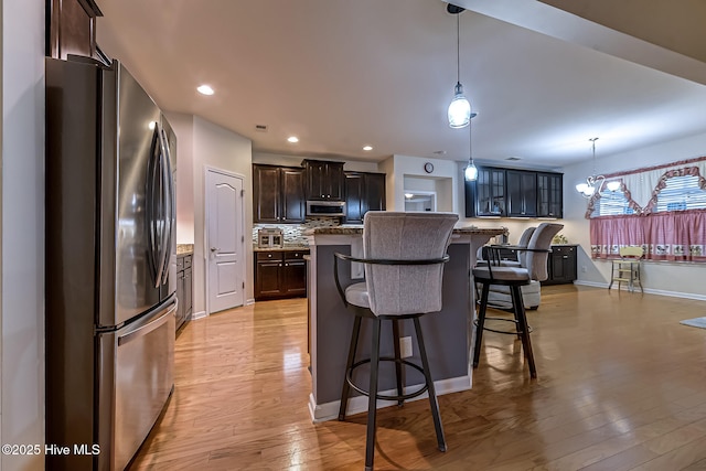 kitchen with stainless steel appliances, dark brown cabinets, hanging light fixtures, and a center island