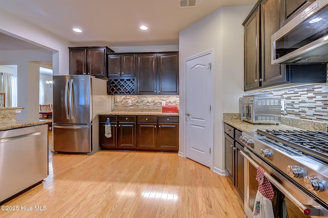 kitchen with appliances with stainless steel finishes, light wood-style flooring, dark brown cabinets, and light stone countertops