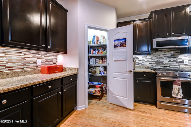 kitchen with stainless steel appliances, decorative backsplash, light wood-style flooring, and light stone counters