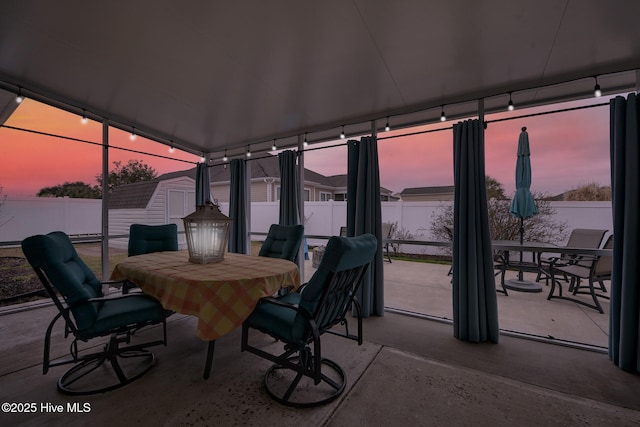 patio terrace at dusk featuring a shed, outdoor dining area, a fenced backyard, and an outbuilding