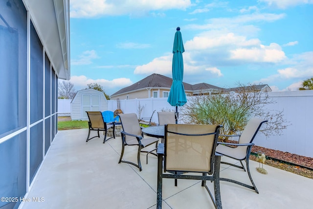 view of patio / terrace featuring outdoor dining area, a fenced backyard, an outdoor structure, and a shed