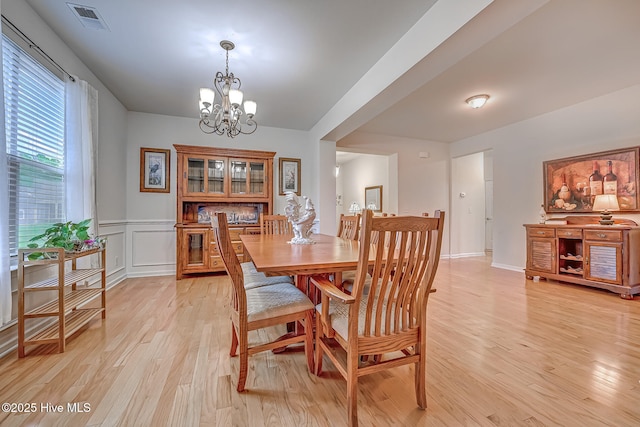 dining room featuring visible vents, wainscoting, light wood-type flooring, a decorative wall, and a notable chandelier