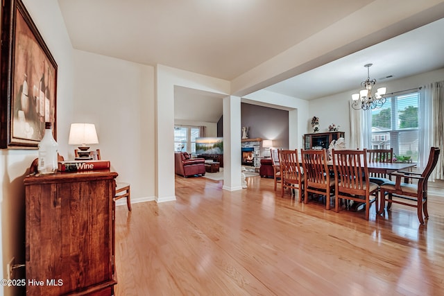 dining room with a fireplace, light wood-style flooring, baseboards, and an inviting chandelier