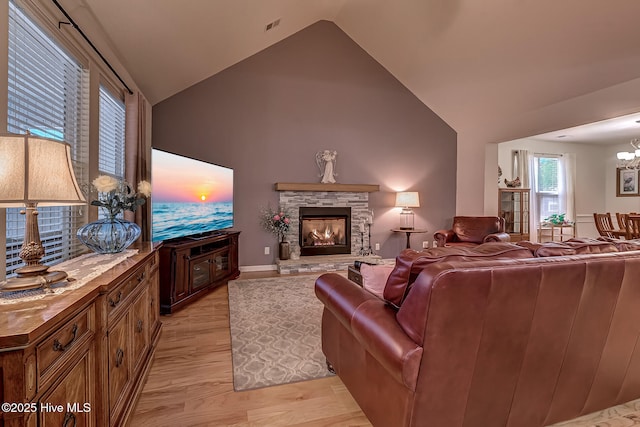 living area featuring visible vents, light wood-style flooring, an inviting chandelier, a stone fireplace, and high vaulted ceiling