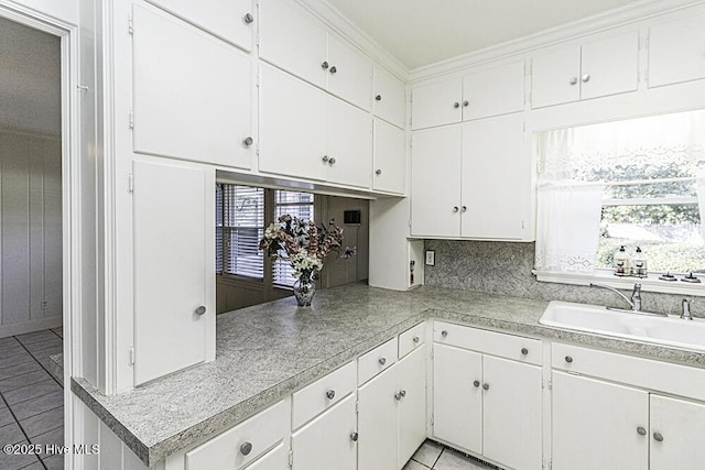 kitchen with light tile patterned floors, a sink, white cabinetry, light countertops, and crown molding