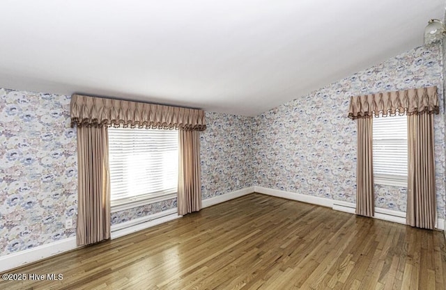 spare room with lofted ceiling, wood finished floors, plenty of natural light, and wallpapered walls