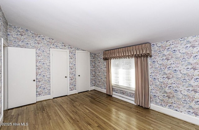 spare room with wood finished floors, vaulted ceiling, baseboards, and wallpapered walls