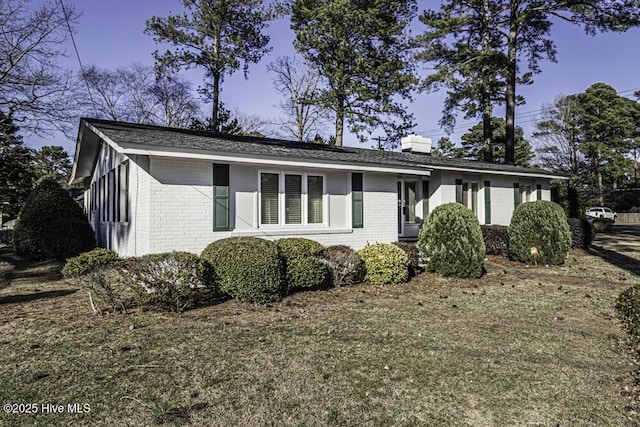 single story home featuring a front yard, brick siding, and a chimney