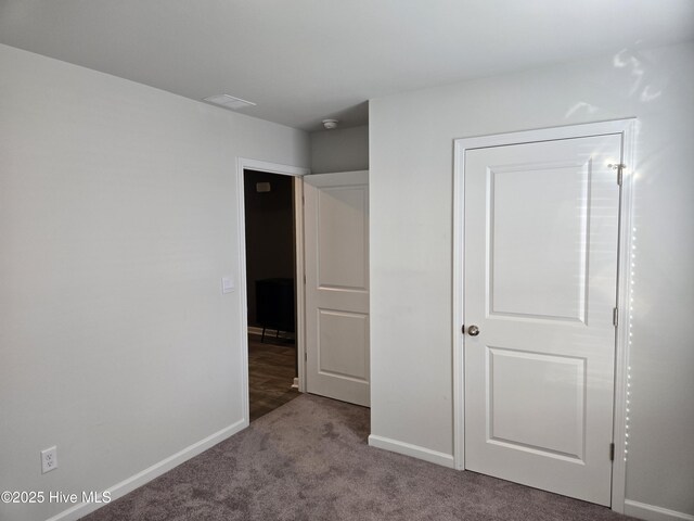 spare room with visible vents, dark carpet, and baseboards