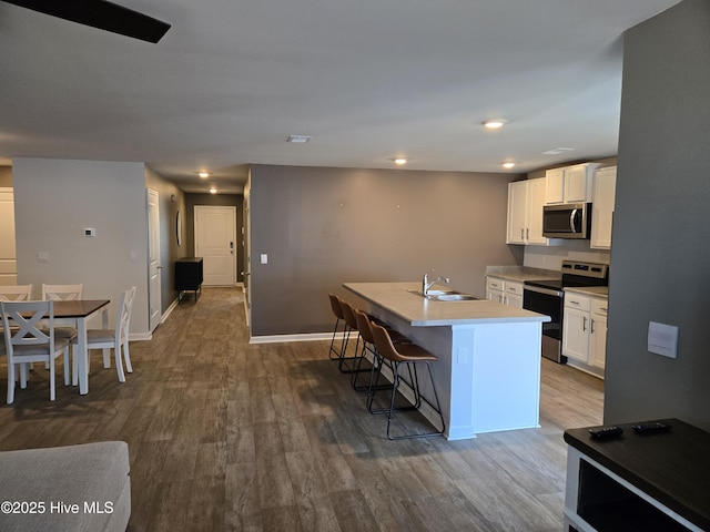 kitchen featuring a kitchen island with sink, stainless steel appliances, light countertops, a kitchen bar, and white cabinetry