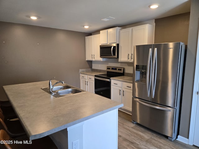 kitchen with appliances with stainless steel finishes, a sink, a kitchen island with sink, and white cabinetry