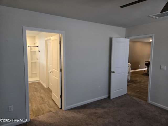 unfurnished bedroom with baseboards, visible vents, dark carpet, and ensuite bath