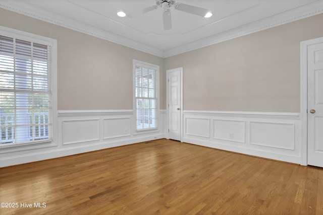 empty room featuring a wainscoted wall, wood finished floors, a ceiling fan, and crown molding