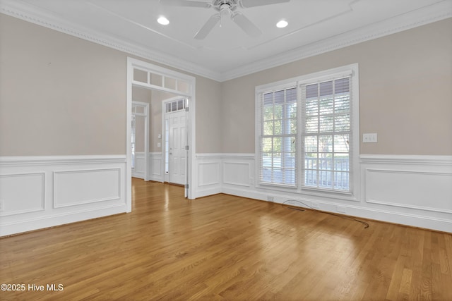 unfurnished room featuring a wainscoted wall, light wood-type flooring, a ceiling fan, and crown molding