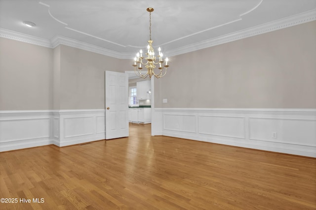 empty room with an inviting chandelier, crown molding, wood finished floors, and a wainscoted wall