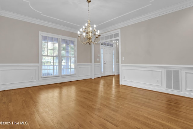 unfurnished dining area featuring a wainscoted wall, a notable chandelier, visible vents, light wood-style floors, and ornamental molding