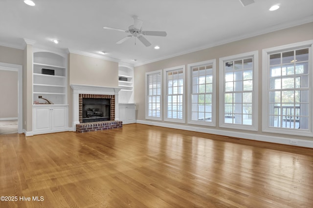 unfurnished living room with built in features, ceiling fan, ornamental molding, light wood-type flooring, and a fireplace