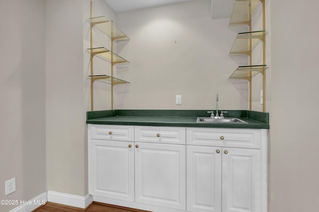 bar with dark wood-style flooring, a sink, and baseboards