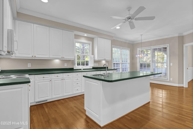 kitchen featuring white cabinets, dark countertops, ornamental molding, wood finished floors, and a sink