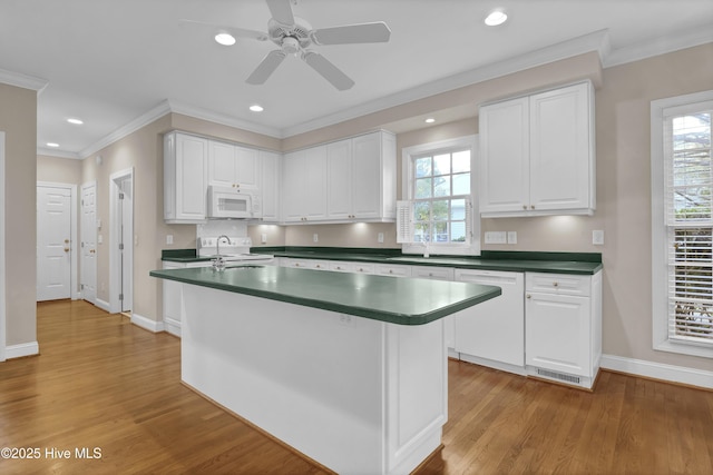 kitchen with white appliances, dark countertops, a healthy amount of sunlight, light wood-type flooring, and white cabinetry