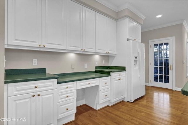 kitchen with white cabinetry, ornamental molding, white fridge with ice dispenser, built in desk, and dark countertops