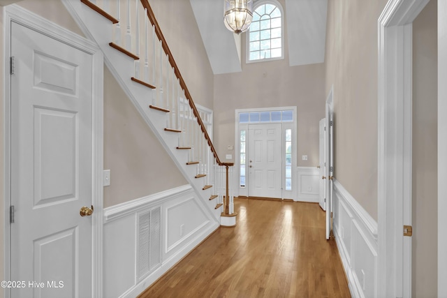 entrance foyer featuring a notable chandelier, visible vents, a decorative wall, light wood-type flooring, and stairs