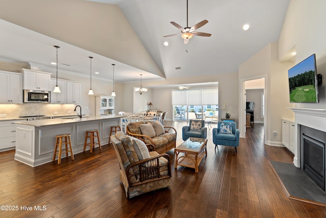 living room with ceiling fan with notable chandelier, a fireplace with flush hearth, and dark wood finished floors