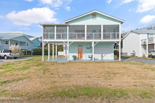 rear view of property with a lawn, an attached garage, and a sunroom